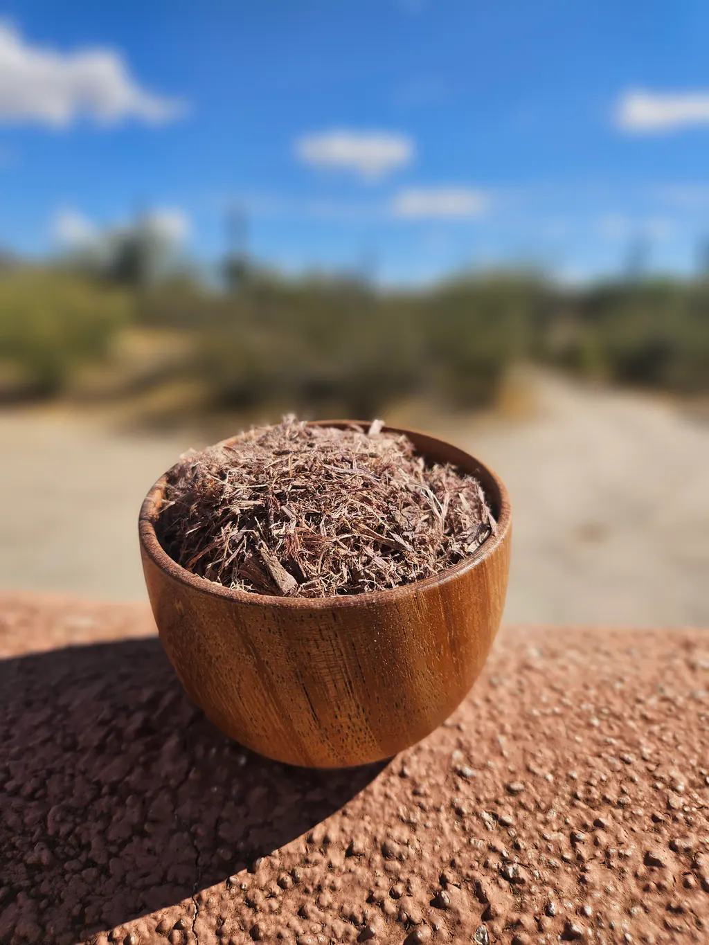 A wooden bowl of shredded Mimosa hostilis root bark outdoors.